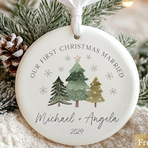 May include: White ceramic Christmas bauble featuring a green watercolour tree design. The bauble reads "Our First Christmas Married" with the names "Michael + Angela" and the year "2024".
