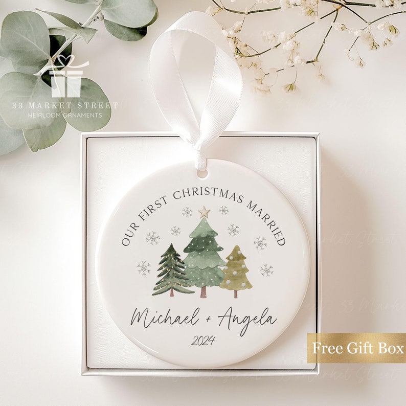 May include: A white ceramic Christmas bauble featuring a green watercolour tree design. The bauble reads "Our First Christmas Married" and "Michael + Angela 2024".