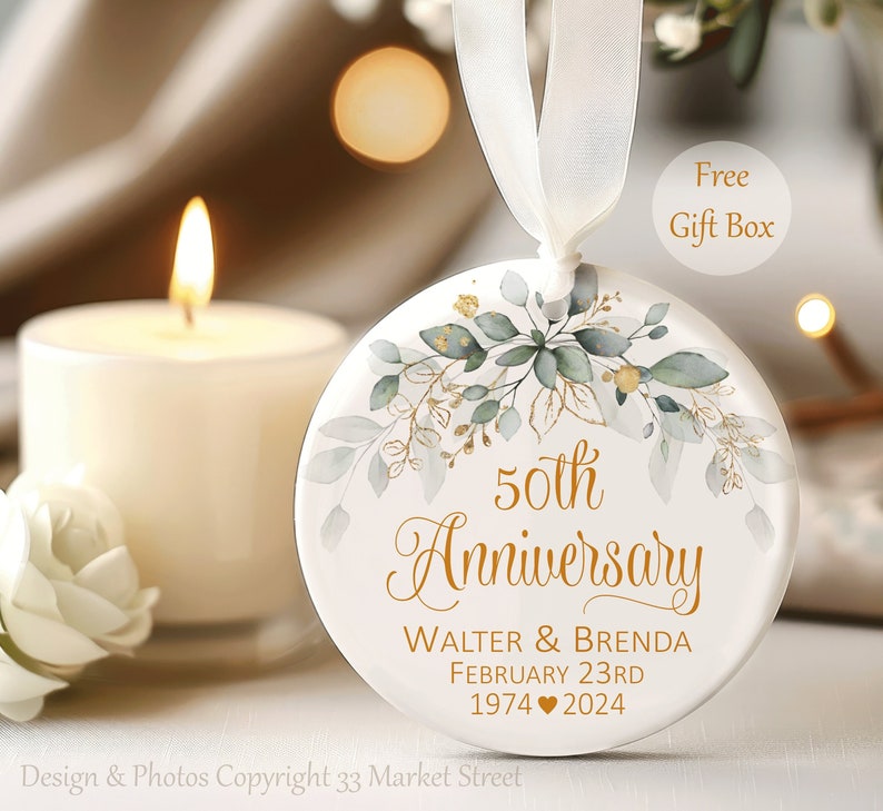 May include: White round ornament with a gold 50th Anniversary design, featuring a watercolor-style floral pattern in shades of green and gold. The text reads "50th Anniversary Walter & Brenda February 23rd 1974 ♥ 2024".
