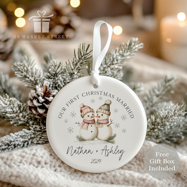 May include: White ceramic Christmas bauble featuring a watercolour illustration of two snowmen. The bauble reads "Our First Christmas Married" with the names "Nathan + Ashley" and the year "2024".
