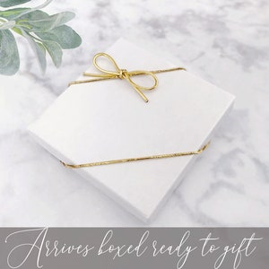 May include: A white gift box tied with a gold ribbon. The box is ready to be given as a gift.