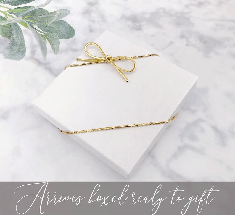 May include: A white gift box tied with a gold ribbon. The box is ready to be given as a gift.