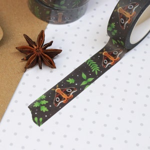 May include: A roll of black washi tape with a repeating pattern of brown moths and green leaves. The tape is on a white background with small gray dots.