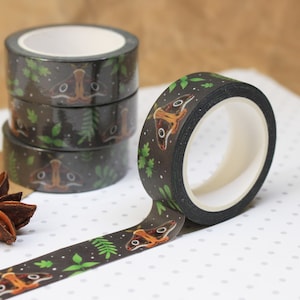 May include: A roll of black and green washi tape with a repeating pattern of brown moths and green leaves. The tape is rolled up and there are three other rolls of the same tape behind it.