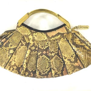 Puede incluir: Un bolso de mano dorado con estampado de piel de serpiente. El bolso tiene un asa superior y un cierre de solapa.