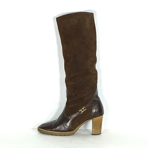 May include: Brown suede knee-high boots with a block heel and a buckle detail on the side.