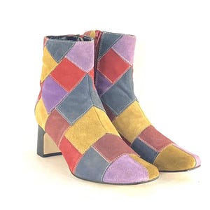 以下が含まれることがあります： カラフルなパッチワークアンクルブーツのペア。ブーツは、赤、紫、青、黄、茶色のスエードの正方形を使用した幾何学模様が特徴です。ブロックヒールとジッパー開閉部があります。