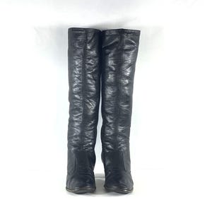 May include: A pair of black knee-high boots featuring a smooth, slightly textured finish. The boots have a tall, structured shaft that reaches the knee, a rounded toe box, and a visible vertical seam running down the center of the front panel.