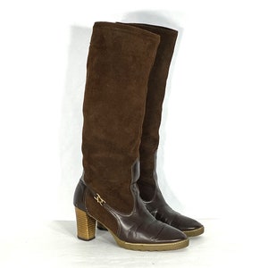 May include: A pair of brown suede knee-high boots with a block heel and a gold buckle detail.