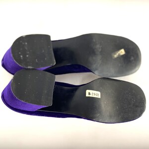 May include: A pair of purple velvet shoes with black soles. The shoes have a low heel and a rounded toe. The soles have a sticker with the number B-1942.