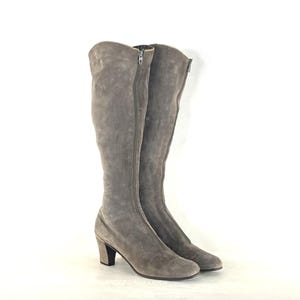 May include: A pair of knee-high grey suede boots with a zip closure. The boots have a rounded toe and a small block heel. The boots are displayed against a white background.