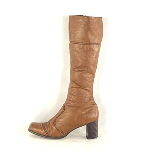 Puede incluir: Una bota alta de cuero marr&oacute;n, con punta cuadrada y tac&oacute;n grueso. La bota presenta una superficie texturizada y costuras decorativas a lo largo de las costuras. El tac&oacute;n mide unos 7,6 cm.
