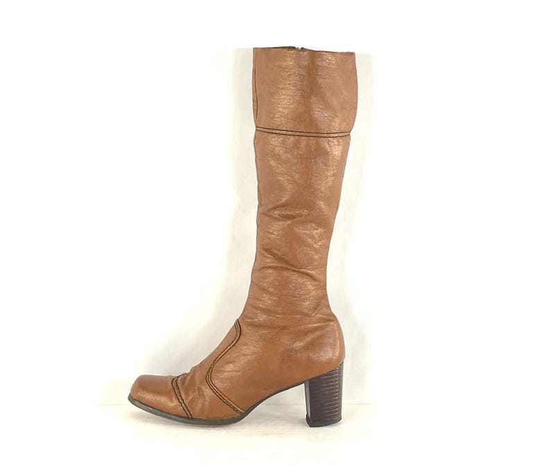 Puede incluir: Una bota alta de cuero marr&oacute;n, con punta cuadrada y tac&oacute;n grueso. La bota presenta una superficie texturizada y costuras decorativas a lo largo de las costuras. El tac&oacute;n mide unos 7,6 cm.
