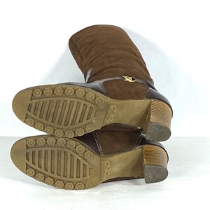 May include: Brown suede knee-high boots with a wooden heel and a rubber sole. The boots have a zipper on the back and a gold buckle on the front.