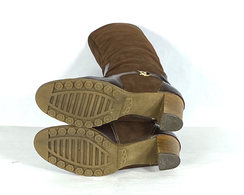 May include: Brown suede knee-high boots with a wooden heel and a rubber sole. The boots have a zipper on the back and a gold buckle on the front.