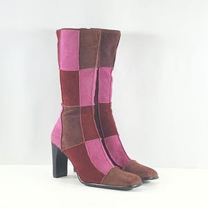 May include: A pair of mid-calf boots featuring a patchwork design of suede panels in shades of dark brown, burgundy, and bright pink. The boots have a square toe silhouette and a solid black block heel, with visible vertical seams connecting the panels.