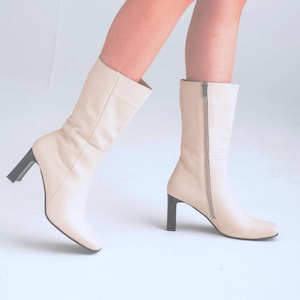 May include: A pair of cream-colored leather boots with a block heel and a zipper on the side.
