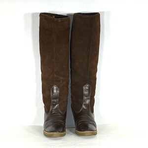 May include: A pair of brown suede knee-high boots with a pointed toe and a low heel.