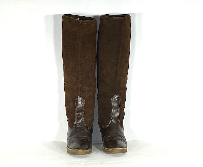 May include: A pair of brown suede knee-high boots with a pointed toe and a low heel.
