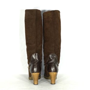 May include: A pair of brown suede knee-high boots with a wooden heel. The boots have a zipper on the inside of the leg and a buckle on the outside.