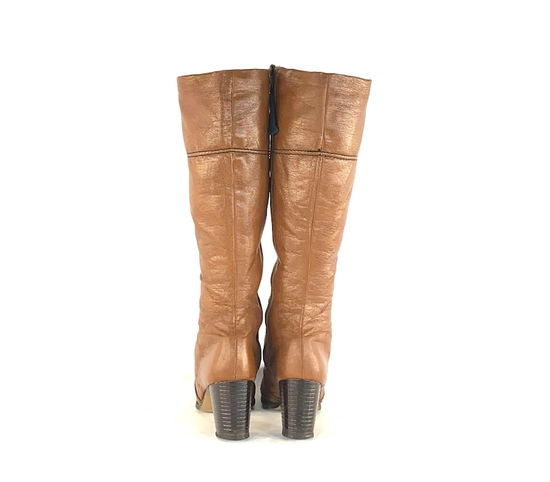 Puede incluir: Un par de botas vintage hasta la rodilla en un tono marr&oacute;n c&aacute;lido. Las botas presentan un aspecto de cuero texturizado, un tac&oacute;n de bloque y cierre de cremallera. Las botas miden unos 38 cm de alto.
