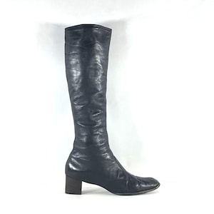 May include: A knee-high black leather boot with a smooth, slightly textured finish and a rounded toe. The boot features a block heel and a streamlined silhouette that extends from the foot up to the calf, showcasing a consistent dark tone.