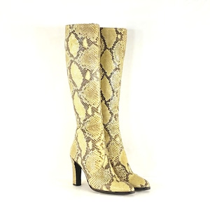 Könnte beinhalten: Kniehohe Stiefel mit Schlangenmuster in Beige-, Braun- und Cremetönen. Die Stiefel haben eine spitze Zehenpartie und einen hohen, schwarzen Absatz. Die Stiefel sind aus einem strukturierten Material. Ca. 40 cm hoch.