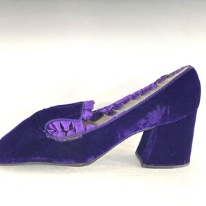 May include: A single, vintage, purple velvet shoe with a block heel. The shoe has a rounded toe and a decorative ruffle detail on the vamp. The heel measures approximately 3 inches.