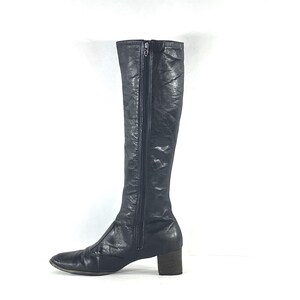 May include: A knee-high black leather boot with a smooth, slightly textured finish. The boot features a full-length vertical zipper along the side, a rounded toe, and a sturdy, block-style heel. The design is sleek, simple, and functional.