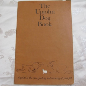 May include: A vintage book titled "The Upjohn Dog Book" with a brown cover. The cover features the title in a serif font and line drawings of dogs. The text "A guide to the care, feeding and training of your pet" is printed at the bottom.