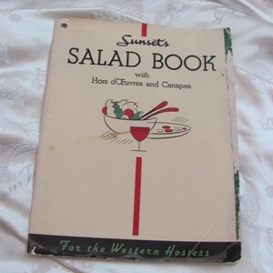 May include: Vintage cookbook titled "Sunset's Salad Book with Hors d'Oeuvres and Canapes" for the Western Hostess. The cover features a red and white illustration of a salad bowl, a glass of wine, and a plate with red dots.