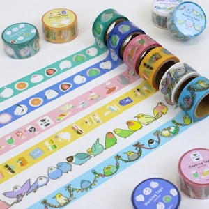 Könnte beinhalten: Eine Sammlung dekorativer Masking-Tape-Rollen mit verschiedenen farbenfrohen Designs. Die Tapes zeigen Muster von Lebensmitteln, Vögeln und anderen niedlichen Illustrationen. Die Rollen sind in Grün-, Blau-, Rosa-, Gelb- und Orangetönen gehalten und tragen die Aufschrift "Masking Tape".
