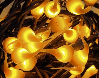 May include: A string of decorative lights featuring numerous small, translucent, amber-colored bulb covers shaped like teardrops or flames. The bulbs are clustered together and attached to dark, intertwined electrical wires, emitting a warm glow.