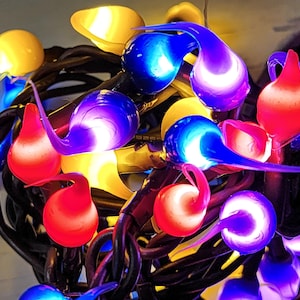 May include: A close-up of a string of colorful lights. The lights are shaped like teardrops and are in shades of red, blue, yellow, and purple. The lights are strung on black wires.