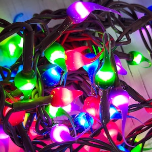 May include: Close-up of a string of colorful Christmas lights. The lights are teardrop-shaped and come in various colors, including red, green, blue, and purple. The wires are dark brown, and the lights are lit up, creating a festive atmosphere.