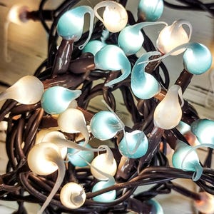 May include: Close-up of a string of decorative lights. The lights have a teardrop shape with a light blue and white color scheme. The lights are connected by dark brown wires, creating a tangled, artistic display.