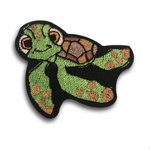 Pode incluir: Patch bordado com uma tartaruga marinha de desenho animado. A tartaruga tem um corpo verde com detalhes marrons e bege em sua carapaça. O patch é contornado em preto e tem uma expressão amigável.