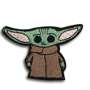 May include: Embroidered patch featuring a green alien character with large eyes and pointed ears. The character is wearing a brown coat. The patch has a black border and is likely for clothing or accessories.