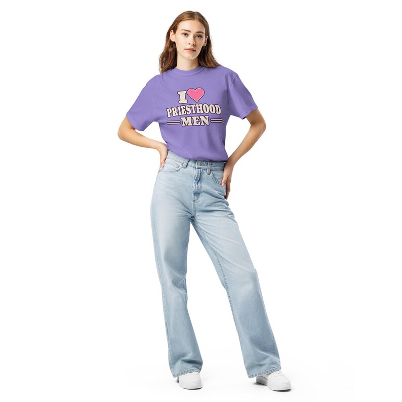 May include: A light purple short-sleeve t-shirt featuring a pink heart icon above the text I PRIESTHOOD MEN in white and dark blue lettering, paired with light blue denim jeans and white sneakers.