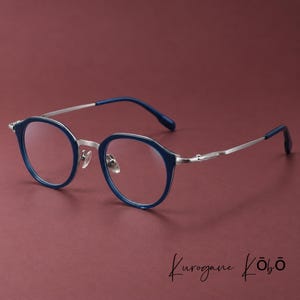May include: Round eyeglasses featuring a deep blue acetate frame front with a silver-toned metal bridge and thin temples. The temple tips are covered in matching blue acetate. The text Kurogane Kōbō is printed in the lower right corner.