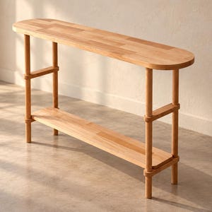 May include: A light-toned wooden console table featuring a smooth, elongated oval top and a matching lower shelf. The structure is supported by four cylindrical legs connected by horizontal wooden bars, creating a clean, open frame design.