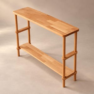 May include: A light-colored wooden console table featuring two rectangular shelves supported by four cylindrical vertical posts. The structure is composed of smooth, natural-toned wood with visible grain patterns, showcasing a clean, open design with rounded edges on the shelves.