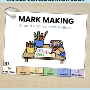 Peut inclure: Un livre de communication partagée Mark Making avec une couverture blanche illustrée d'un bureau, de fournitures artistiques et d'une main qui dessine. La section inférieure comporte des onglets colorés Core Words, Who, What doing, What, Where, What like.