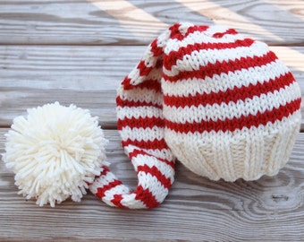 May include: A red and white striped knitted hat with a long, pointed top and a white pom-pom on the end.