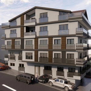 May include: A multi-story apartment building with a light gray facade, dark brown vertical accents, and glass-railed balconies. The structure features multiple windows and is situated next to a paved road with several parked cars.