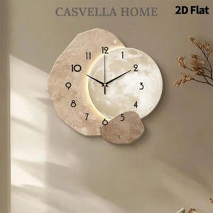 May include: A wall clock featuring a textured, beige, irregular-shaped base and a circular, illuminated moon-like face. The clock displays black Arabic numerals from 1 to 12 and black hands. The text CASVELLA HOME and 2D Flat appear above.