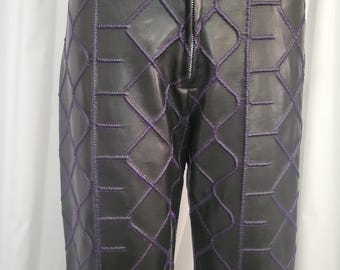 Könnte beinhalten: Schwarze Hose mit einem markanten, violett gestickten Gittermuster auf der Vorderseite. Die Hose verfügt über einen mittigen Reißverschluss aus silberfarbenem Metall, Gürtelschlaufen am Bund und vertikale Nähte, die das geometrische Design bilden.