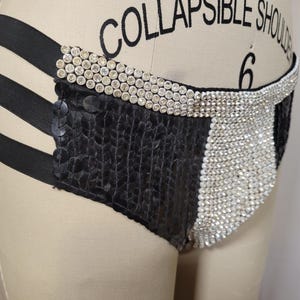 May include: Black and silver sequined underwear with a high-waisted design. The garment features a combination of black sequined fabric and silver rhinestone embellishments, with black elastic straps and a rhinestone-studded waistband.