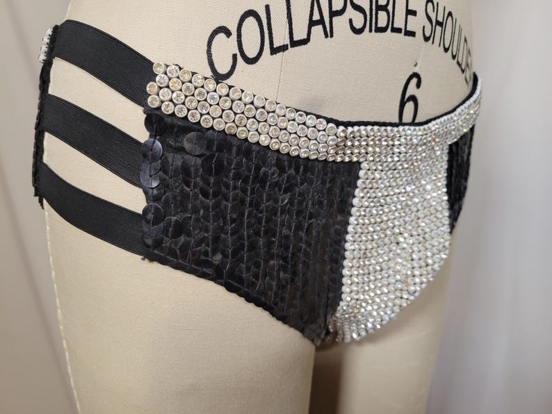 May include: Black and silver sequined underwear with a high-waisted design. The garment features a combination of black sequined fabric and silver rhinestone embellishments, with black elastic straps and a rhinestone-studded waistband.