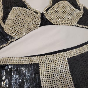 May include: Black sequined bikini set with silver rhinestone accents. The top features a triangle design with rhinestone-covered cups and trim. The bottoms have a sequined design with rhinestone detailing.